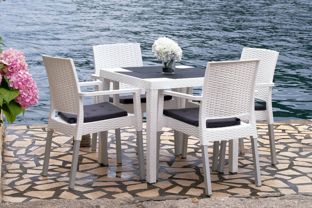 Lege zithoek in de zomer in recreatie aan zee. Witte tafel en fauteuils op terras van zomercafé. Restaurant bedrijf wacht op bezoekers. - Foto, afbeelding