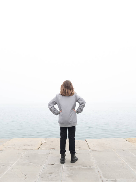 Dziewczyna dziecko patrząc na szary odległy horyzont w oceaniczny mglisty dzień. - Zdjęcie, obraz