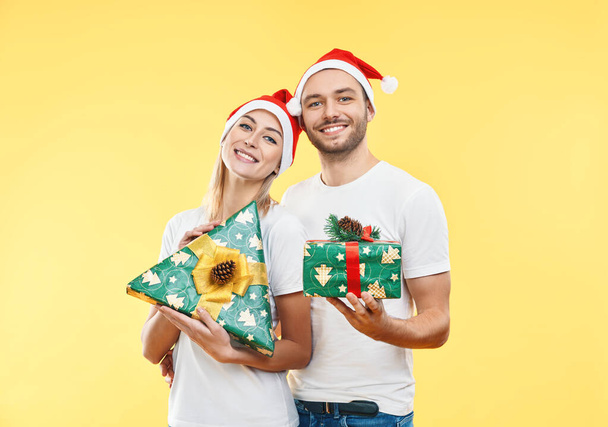 Joven pareja feliz con cajas de regalo de Navidad sobre fondo amarillo - Foto, Imagen