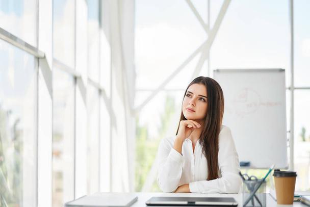 Confident pretty businesswoman in a bright modern office looking to copy space - Φωτογραφία, εικόνα