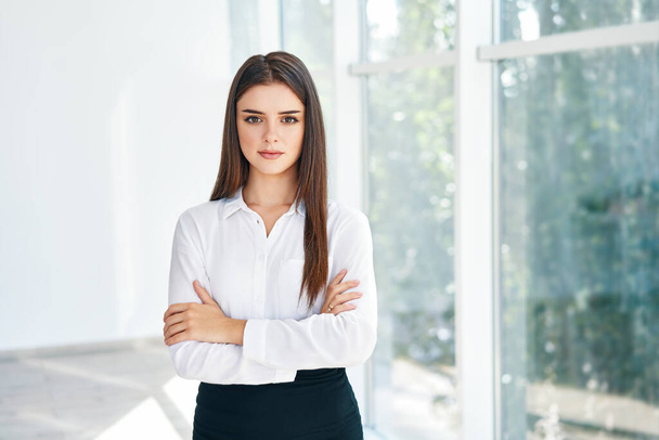 Smiling confident pretty businesswoman with crossed arms posing in a modern office with copy space - Фото, зображення