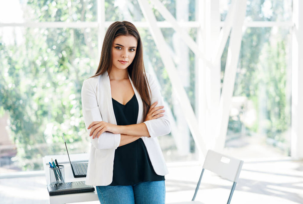 Smiling confident pretty businesswoman with crossed arms posing in a modern office - Foto, Imagen