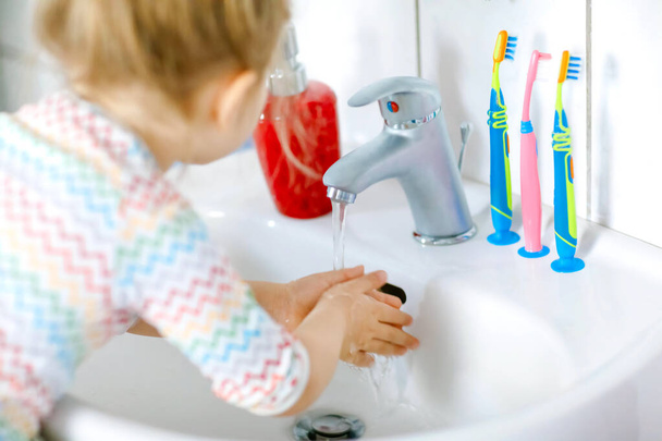 Küçük bir kızın banyoda ellerini sabunla ve suyla yıkaması. Çocuğun vücut parçalarını temizlemeyi öğrenmesini kapat. Virüs salgını sırasında yapılan hijyen rutini. Çocuk evde ya da çocuk odasında.. - Fotoğraf, Görsel