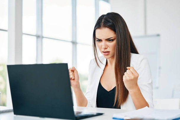 Shocked businesswoman looking at laptop reading bad news at her desk in modern office - Foto, Imagem