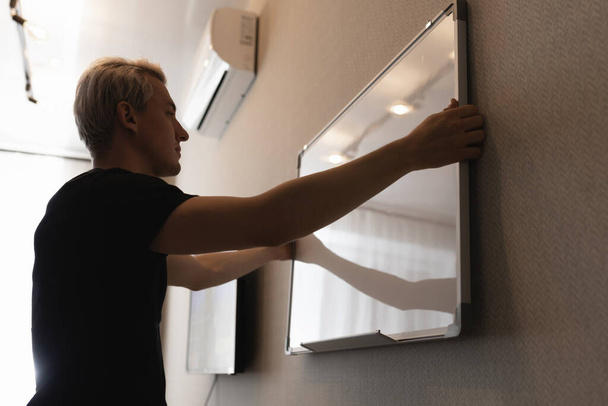 A man hangs a white board on the wall - Fotoğraf, Görsel