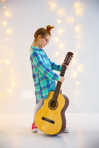 Emotional little girl with guitar in studio. Charming beauty plays the guitar with a slight smile on her face - Fotó, kép