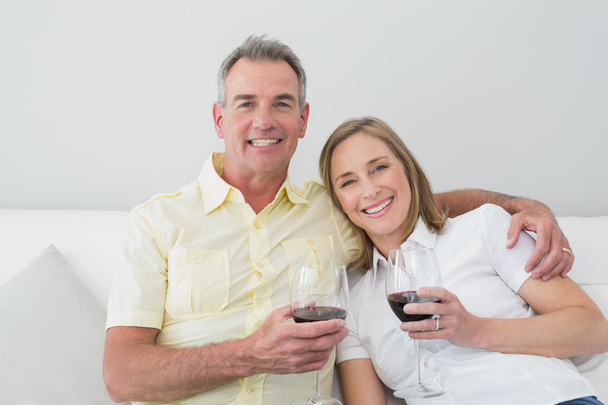 Happy couple with wine glasses sitting on sofa - Fotó, kép