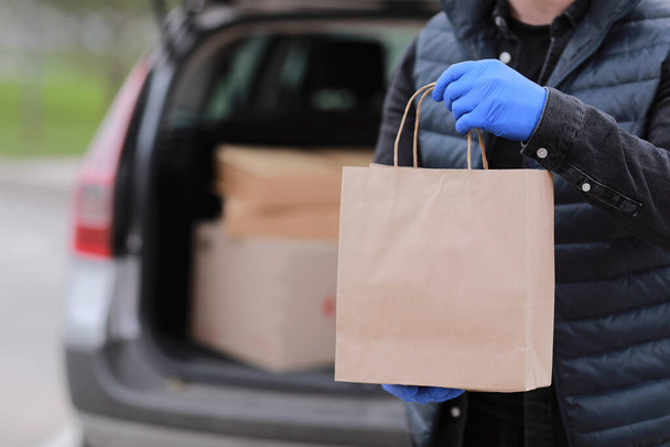 Zusteller in Handschuhen halten Papiertüte in der Nähe des Autos im Freien. Service Coronavirus. Online-Shopping. Attrappe - Foto, Bild