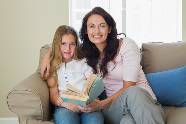 Mother and daughter holding book on sofa - Valokuva, kuva