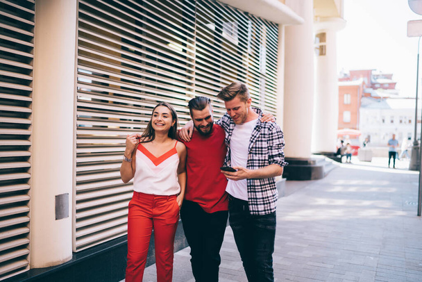Group of young Caucasian men and woman walking at urban setting using cellphone gadget for tracking gps, happy male and female best friends in casual wear enjoying together pastime at city street - Foto, afbeelding