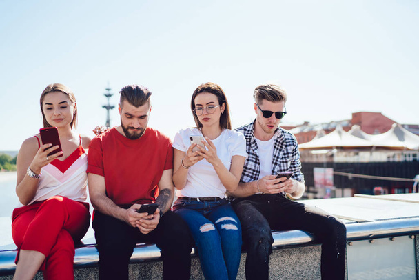 Group of millennial hipster guys in trendy clothes using cellphone device for sharing media files connected to bluetooth, youthful Generation Z ignoring live communication during double date - Fotó, kép