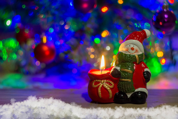 новорічний святковий фон сніговик в капелюсі зі свічкою на дерев'яній дошці снігова ялинка різдвяні кульки розмитий фон крупним планом
 - Фото, зображення