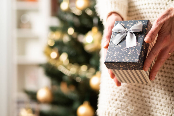 χέρι κρατώντας χριστουγεννιάτικο δώρο κουτί μπροστά από τα φώτα των διακοπών - Φωτογραφία, εικόνα