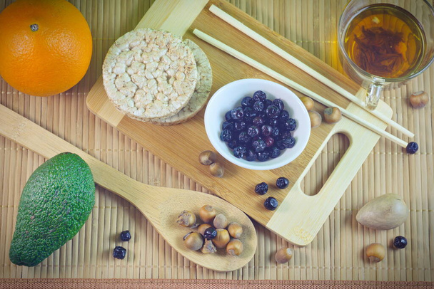 Концепция Flatley здоровое питание пять зерновых хлебов авокадо яблоки chokeberry оранжевые ломтики орехи на деревянном бамбуковом фоне - Фото, изображение