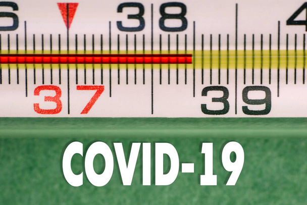 Nahaufnahme eines Hochtemperaturthermometers mit COVID-19 Text. Anzeichen einer Coronavirus-Erkrankung. Virale Symptome. Kontrollen der Körpertemperatur. - Foto, Bild