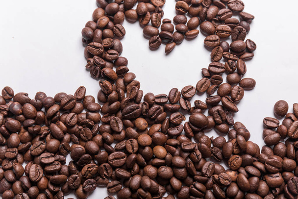 gebrande koffiebonen van verschillende tinten bruin, verspreid over een wit oppervlak dat een hart vormt. Koffie achtergrond of textuur concept en liefde voor koffie. - Foto, afbeelding