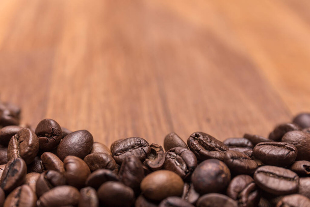 中央の選択的フォーカス、茶色の異なる色合いのコーヒー豆は、専用の木製の表面に散在し、上部に書くためのスペース。コーヒーの背景や食感のコンセプト. - 写真・画像