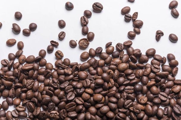 καβουρδισμένοι κόκκοι καφέ διαφόρων αποχρώσεων του καφέ διάσπαρτοι σε λευκή επιφάνεια. Πλαίσιο ή έννοια υφή καφέ - Φωτογραφία, εικόνα