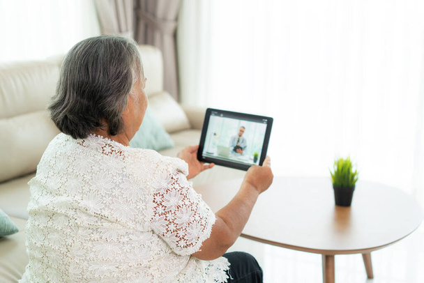 Rückansicht einer älteren Frau, die mit ihrem Arzt Videotelefonie führt, während sie sich zu Hause krank fühlt, auf einem digitalen Tablet Online-Beratung im Gesundheitswesen mit digitaler Technologie.  - Foto, Bild