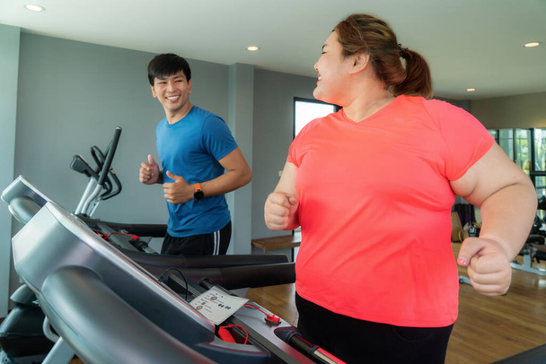 Двоє азіатських тренерів і жінка з надлишковою вагою, які тренуються на біговій доріжці в спортзалі, під час тренувань підстрибують до неї, щоб досягти хороших результатів. Товсті жінки дбають про здоров "я і хочуть схуднути. - Фото, зображення