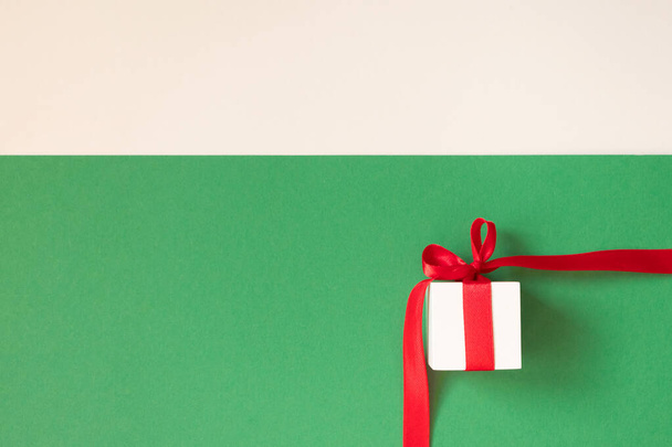 Bílá dárková krabice s červenou stuhou na zeleném a béžovém pozadí - Fotografie, Obrázek