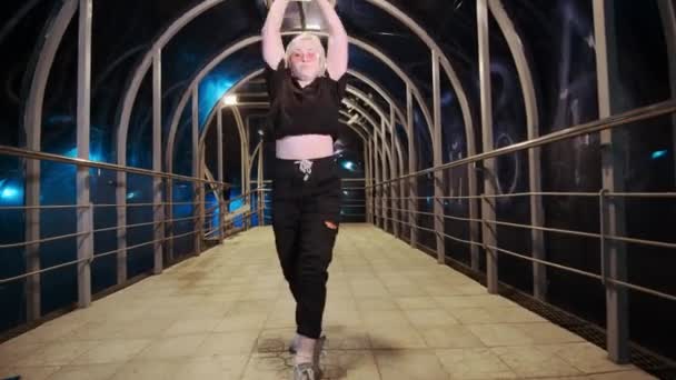 Stijlvolle jonge vrouw dansend hip hop, freestyle of swag 's nachts op overhead voetgangers kruising met verlichte - Video