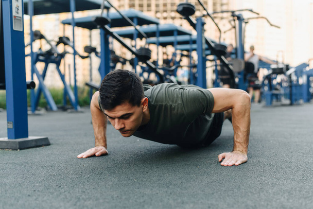 Young man doing push ups outdoor. Young handsome runner warming up and doing some push ups as part of his training. Action and healthy lifestyle concept - Photo, Image