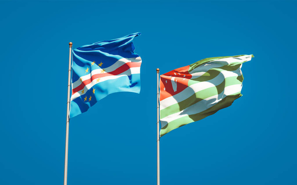 Gyönyörű nemzeti zászlók Abházia és a Zöld-foki-szigetek együtt az ég hátterében. 3D-s művészeti koncepció. - Fotó, kép