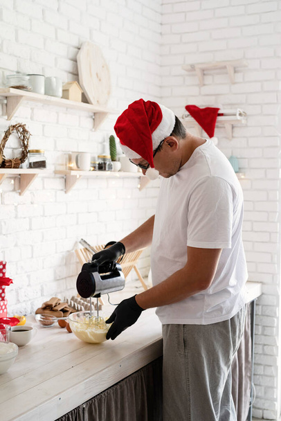 Vánoční vaření. Šéfkuchař v Santa klobouk vaření dezert v kuchyni wipping cream - Fotografie, Obrázek
