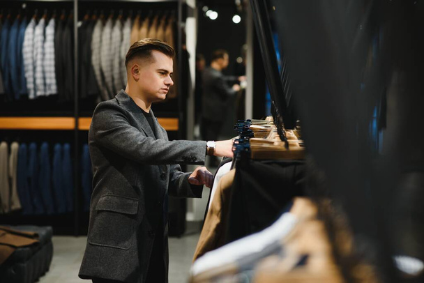 client is an elegant guy looking at the price tag of a suit jacket in a classic costume store on a hanger. - Foto, imagen
