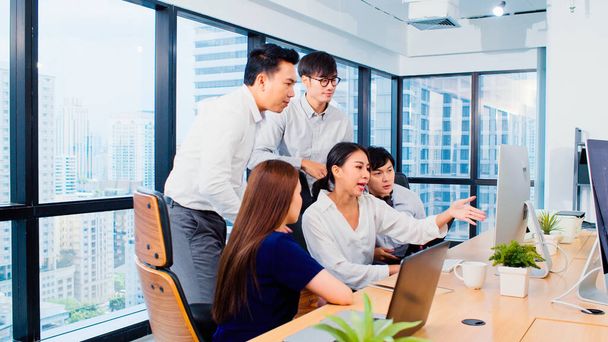 Group of Asian business people work together in team brainstorm discussion on desktop computer in office. Corporate business, coworker teamwork, or financial consultant meeting concept - Photo, Image