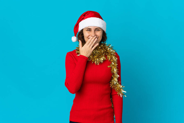 Angielski dziewczyna w Boże Narodzenie kapelusz izolowane na niebieskim tle szczęśliwy i uśmiechnięty pokrycie usta z ręki - Zdjęcie, obraz