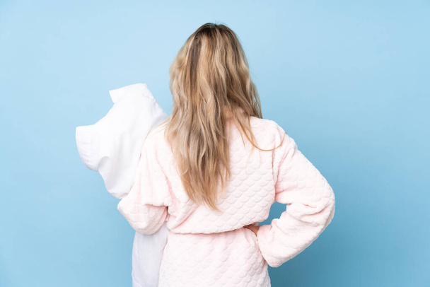 Teenager Russian girl in pajamas isolated on blue background in back position - 写真・画像