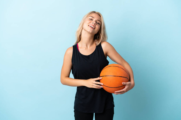 Молода російська жінка грає в баскетбол ізольовано на синьому фоні сміється - Фото, зображення