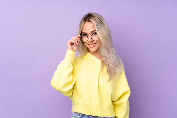 Ragazza adolescente indossa una felpa gialla su sfondo viola isolato con occhiali e felice - Foto, immagini