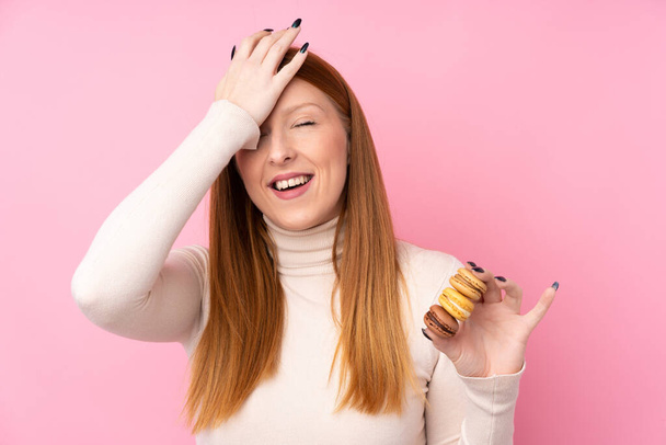 Young redhead woman over isolated pink background holding colorful French macarons and intending the solution - Photo, Image