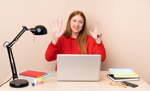 Young student woman in a workplace with a laptop counting seven with fingers - Photo, Image