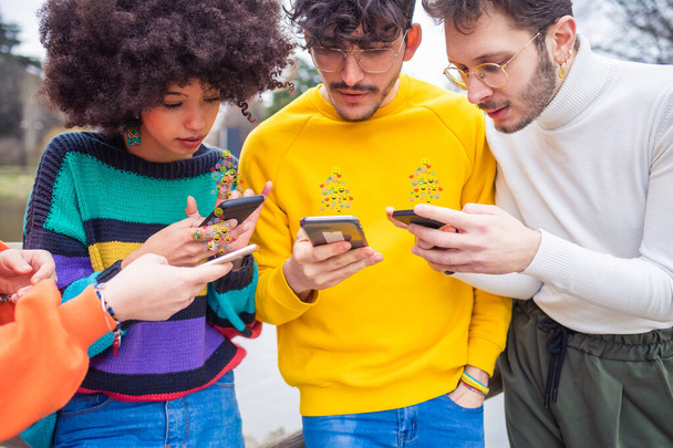 Gruppo di amici multietnici millennials utilizzando i telefoni cellulari - Giovani dipendenti dalle tendenze tecnologiche che seguono e chattano utilizzando emoji ed emoticon - social media, dipendenza, concetto di chat - Foto, immagini