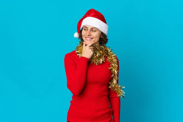 English girl with christmas hat isolated on blue background looking to the side and smiling - Photo, Image
