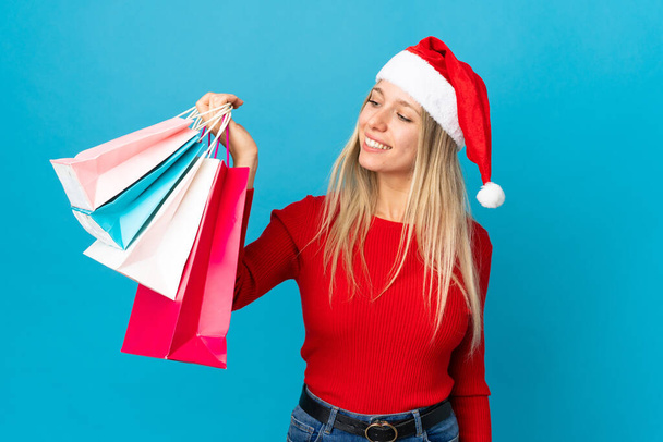 Woman with christmas hat going to buy something isolated on blue background with happy expression - Φωτογραφία, εικόνα