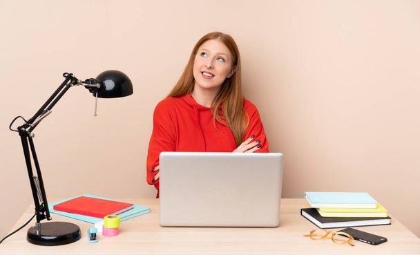 Jovem estudante mulher em um local de trabalho com um laptop olhando para cima enquanto sorri - Foto, Imagem