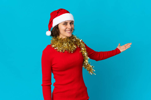 Englisches Mädchen mit Weihnachtsmütze auf blauem Hintergrund, das die Hände zur Seite ausstreckt, um zum Kommen einzuladen - Foto, Bild