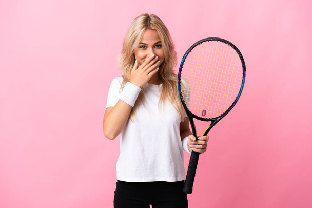 Junge russische Frau spielt Tennis isoliert auf lila Hintergrund glücklich und lächelnd bedeckt Mund mit Händen - Foto, Bild