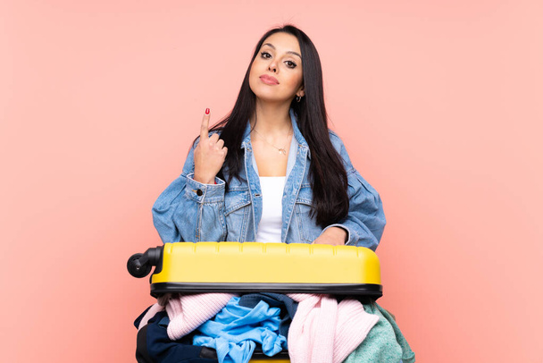 Ταξιδιώτισσα Κολομβιανή με μια βαλίτσα γεμάτη ρούχα πάνω από απομονωμένο ροζ φόντο που δείχνει με το δείκτη μια μεγάλη ιδέα - Φωτογραφία, εικόνα