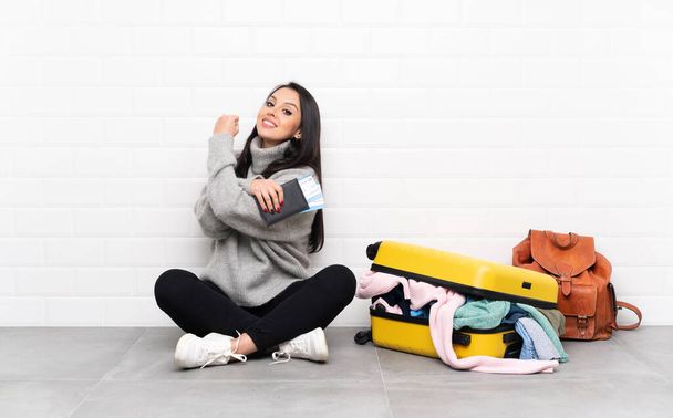 Ταξιδιώτρια Κολομβιανή με μια βαλίτσα γεμάτη ρούχα να κάθεται στο πάτωμα κάνοντας μια δυνατή χειρονομία - Φωτογραφία, εικόνα