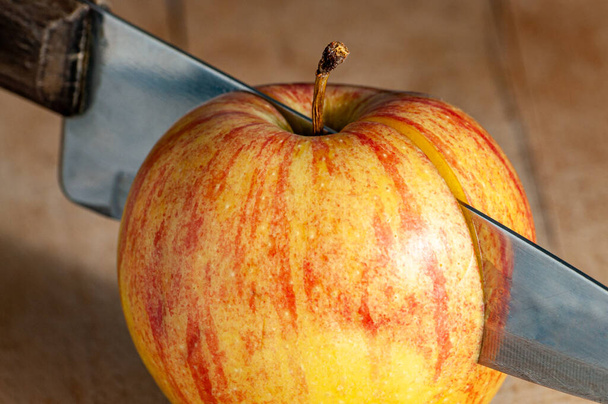 κοντινό πλάνο μαχαιριού κολλημένου σε φρέσκο κόκκινο και κίτρινο μήλο - Φωτογραφία, εικόνα