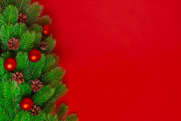 飽和した背景に松のコーンと赤いボールを持つクリスマスツリーの枝からのポストカード、コピースペース - 写真・画像