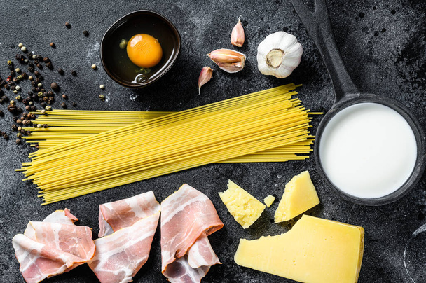 Zutaten für traditionelle italienische Pasta alla carbonara. Ungekochte Spaghetti, Bauchspeck, Parmesan, Ei. Schwarzer Hintergrund. Ansicht von oben. - Foto, Bild