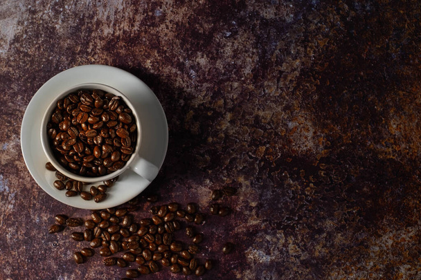 Top view above of Black coffee seed for morning menu in white ceramic cup with coffee beans roasted on old rusty table background. Flat lay with copy space. - Foto, imagen