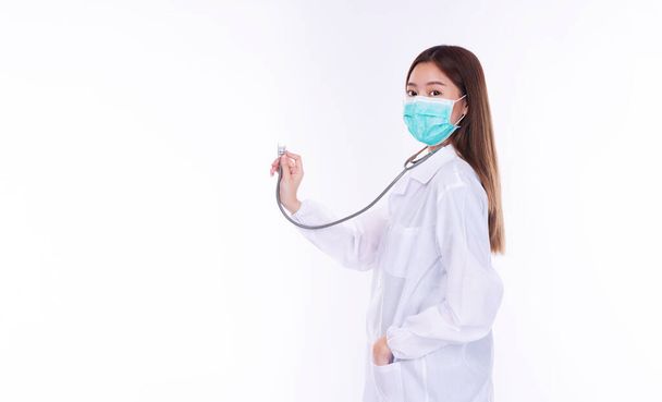 Mask to prevent virus concept Friendly young woman doctor or nurse wear coat uniform and face mask while holding stethoscope and checking hear pulse over isolated on white background. - Foto, afbeelding